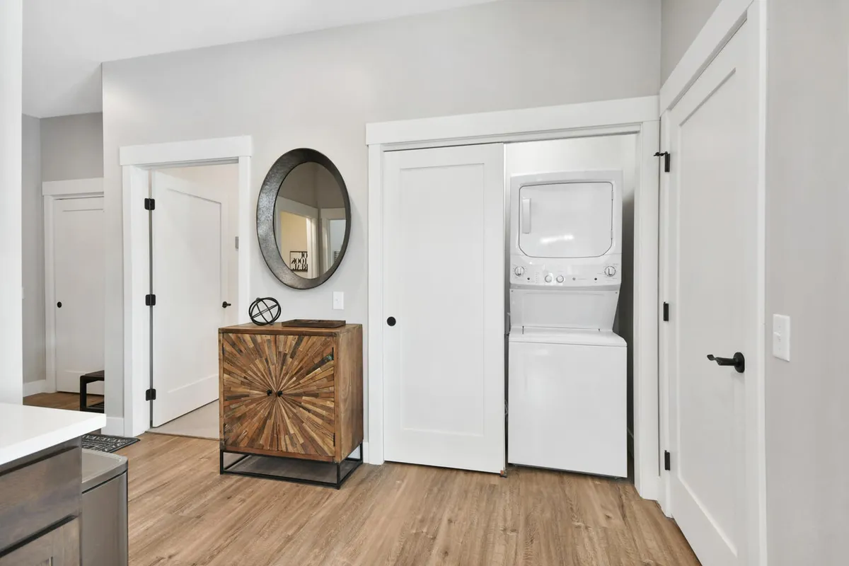 A functional laundry area with modern appliances, a textured cabinet, and a round mirror, all arranged for ease of use and visual appeal. The space is bright and organized, making everyday tasks convenient and pleasant.
