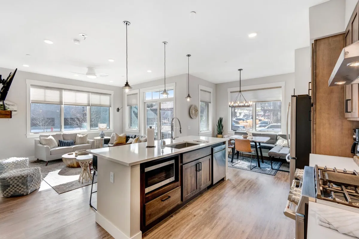 This image captures an open-concept kitchen, living, and dining area. The kitchen island is central, with modern seating, and flows directly into a comfortable living space with inviting sofas and a dining table nearby. The space exudes warmth and togetherness, with soft lighting and a cozy, welcoming vibe.
