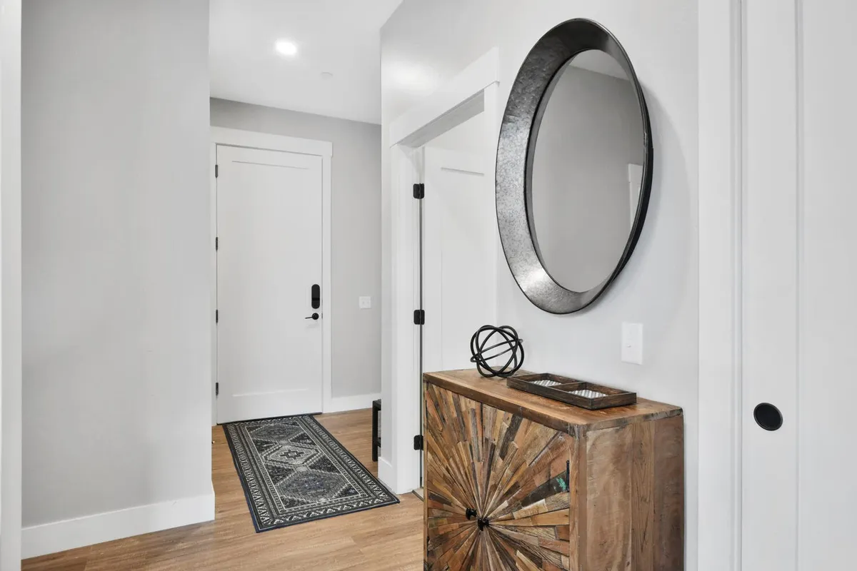 A stylish entry area with a wooden cabinet, decorative mirror, and area rug, creating a welcoming space for guests as they arrive. The combination of warm lighting and tasteful decor sets a positive first impression and hints at the thoughtful design throughout the condo.