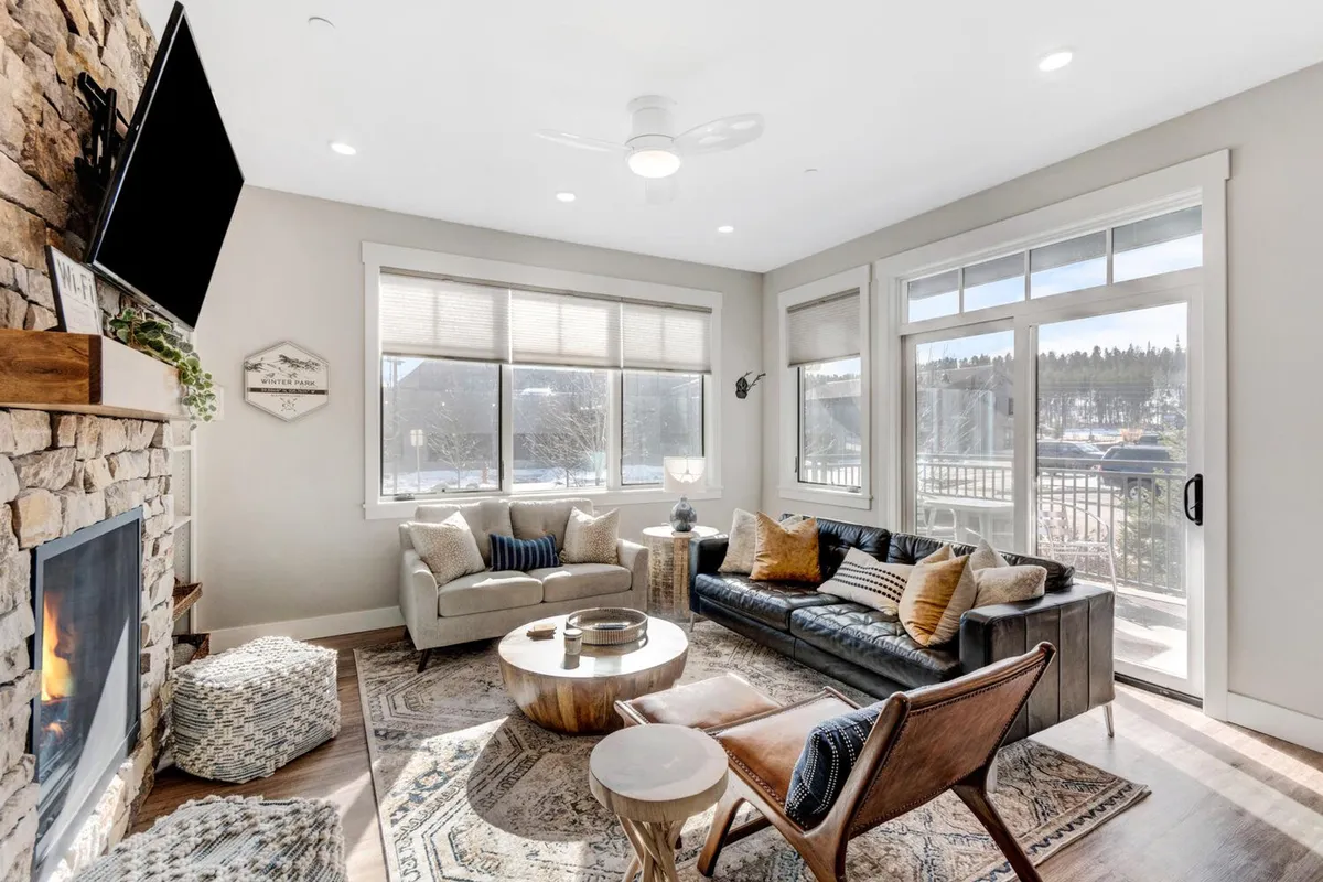 A warm, welcoming living room featuring a fireplace, sofa, rug, and prominent large windows that suggest access to natural light and potentially outdoor views. The cozy setup invites both people and pets to unwind and enjoy time together inside after adventure-filled days.