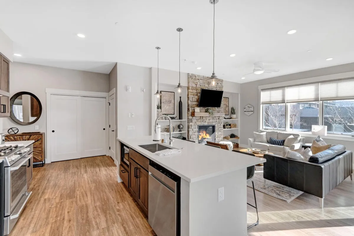 A wide-angle view of the main living area, featuring a spacious kitchen island, a modern fireplace, and a plush living room seating area. The scene is set for entertaining or relaxing, with elegant finishes and a warm, inviting color palette.