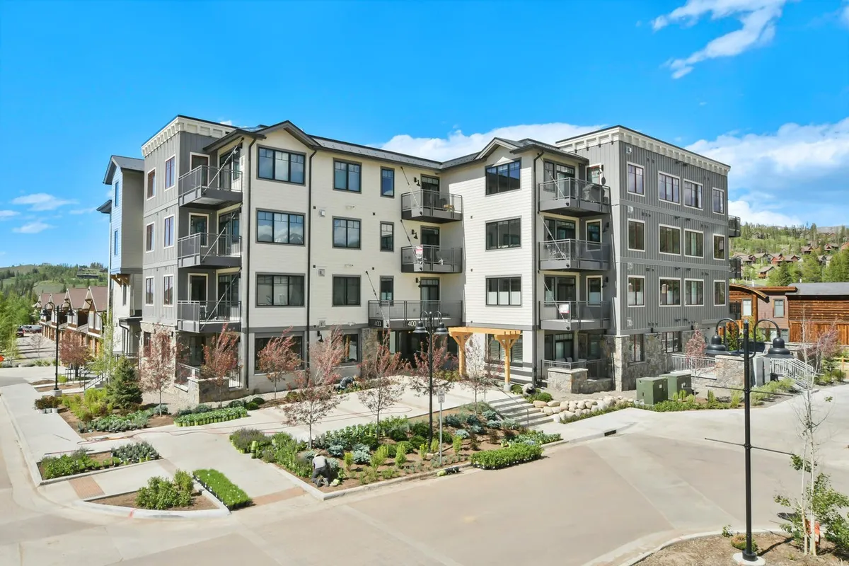 The exterior of a modern condo building featuring landscaped gardens, sunlit balconies, and residents strolling through the neighborhood. The scene captures the lively, walkable character of downtown Winter Park, showing how close the building is to community amenities and events.