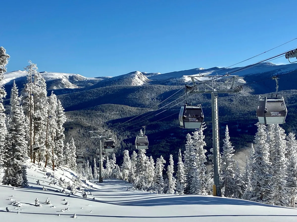This image captures ski lift gondolas gliding above snow-covered trees with distant mountains on the horizon. The landscape is blanketed in snow, evoking excitement for winter sports like skiing and snowboarding, and hints at the breathtaking alpine environment.